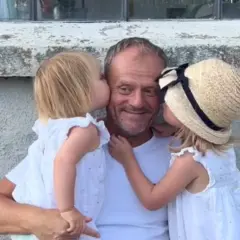 Donald Tusk z dwiema córkami całującymi go w policzki.