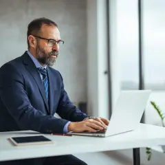 Biznesmen w garniturze analizuje, czy ustawa o wakacjach składkowych zostanie rozszerzona na większe przedsiębiorstwa, pracując przy laptopie.