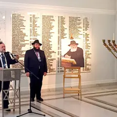 Dwóch mężczyzn w strojach religijnych, tablica z nazwiskami i menora.