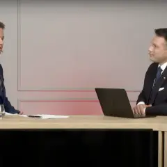 Sławomir Mentzen w garniturze siedzi przy biurku z laptopem, rozmawiając z drugim mężczyzną. Czy to dowód, dlaczego Sławomir Mentzen unika debat z kandydatami Koalicji Obywatelskiej?