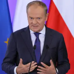 Donald Tusk w garniturze przemawia przed flagami Polski i Unii Europejskiej.