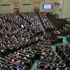 Posiedzenie Sejmu RP, wielu posłów siedzi w ławach, na mównicy przemawia mężczyzna.