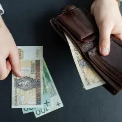 Ręce trzymają polskie banknoty i brązowy portfel. Czy to początek wzrostu renty alkoholowej o 5% od marca 2026?