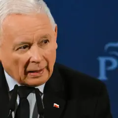 Jarosław Kaczyński, w garniturze z polską flagą, przemawia na tle logo PiS. Czy Jarosław Kaczyński faktycznie planuje oddać władzę młodszym politykom?