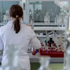 Naukowczyni w białym fartuchu pracuje w laboratorium z probówkami i odczynnikami.