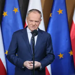 Premier przemawia na tle flag Polski i UE. Sondaże nie dają pewności, czy rząd koalicyjny przetrwa 2026 rok w niezmienionym składzie.
