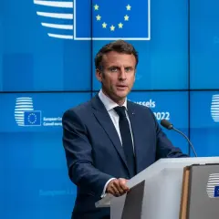 Emmanuel Macron w garniturze przemawia za mównicą na tle niebieskiej ściany z logo Unii Europejskiej.