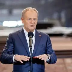 Donald Tusk w garniturze przemawia przy mikrofonie.