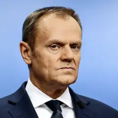 Portret Donalda Tuska w granatowym garniturze i białej koszuli na jasnoniebieskim tle.