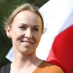 Uśmiechnięta żona Hołowni, niczym pilotka, patrzy w dal na tle biało-czerwonej flagi.