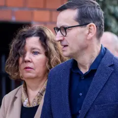 Iwona i Mateusz Morawieccy w zbliżeniu, na tle ceglanego muru.