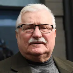 Lech Wałęsa w okularach i z wąsami, w swetrze i marynarce. W tle niewyraźne postacie.
