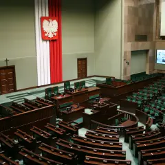 Sala plenarna Sejmu RP z godłem Polski i rzędami zielonych foteli.