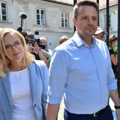 Małgorzata Trzaskowska w jasnej marynarce i Rafał Trzaskowski w błękitnej koszuli otoczeni przez dziennikarzy.