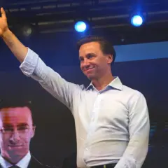 Mężczyzna w jasnej koszuli pozdrawia tłum. Na ekranie za nim widać twarz polityka, który mógłby mieć tyle lat, ile ma Bosak.