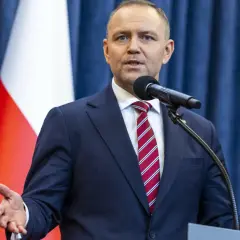 Mężczyzna w garniturze przemawia przy mikrofonie na tle flagi Polski. Czy prezydent faktycznie planuje ogłosić stan wyjątkowy w związku z sytuacją na wschodzie?