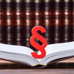 Czerwony znak paragrafu na otwartej księdze na tle regałów z książkami prawniczymi.