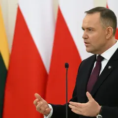 Karol Nawrocki, w garniturze, przemawia na tle flag. Jego gestykulacja i pewność siebie mogą być powodem, dlaczego Karol Nawrocki stał się nowym liderem sondaży zaufania na prawicy.