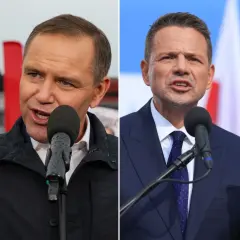 Dwaj mężczyźni w garniturach przemawiający do mikrofonów na tle flag.