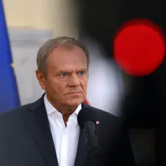 Donald Tusk w garniturze, z flagą UE w tle i czerwonym światłem.