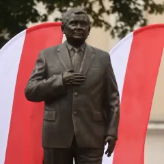 Pomnik Lecha Kaczyńskiego, jednego z wielu w Polsce, stoi na tle biało-czerwonych flag.