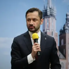 Tobiasz Bocheński, z mikrofonem w dłoni, przemawia na tle krakowskich wież. Jego rosnąca popularność sprawia, że jest uznawany za "czarnego konia" w wyścigu o urząd prezydenta.