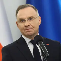 Prezydent Andrzej Duda w garniturze przed mikrofonem, w tle flagi Polski i UE.