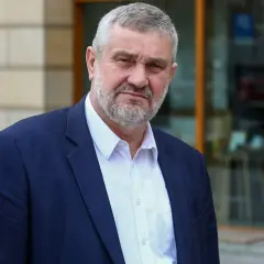 Mężczyzna z siwą brodą w granatowej marynarce i białej koszuli. Czy pozna prawdę o zarzutach prokuratorskich dla byłego ministra rolnictwa w 2025 roku?
