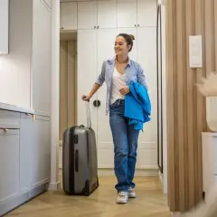 Kobieta z walizką w nowoczesnym mieszkaniu. Zmiany w prawie mogą wpłynąć na to, dlaczego wspólnoty mieszkaniowe będą mogły podnosić czynsz za najem krótkoterminowy.
