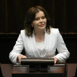 Anna Krupka w białej marynarce przy mównicy. Czy wiceprezes PiS nie dostaje pieniędzy za funkcję?
