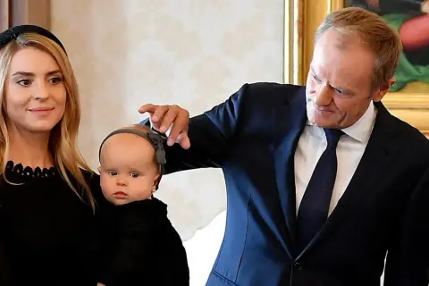 Kasia Tusk z dziećmi, Donald Tusk delikatnie dotyka główki niemowlaka.