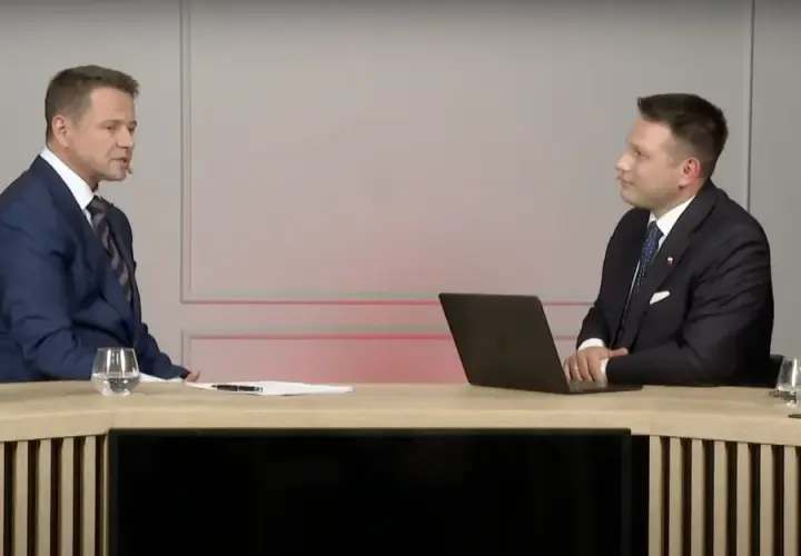 Sławomir Mentzen w garniturze siedzi przy biurku z laptopem, rozmawiając z drugim mężczyzną. Czy to dowód, dlaczego Sławomir Mentzen unika debat z kandydatami Koalicji Obywatelskiej?
