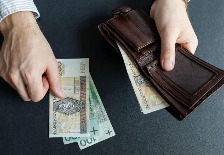 Ręce trzymają polskie banknoty i brązowy portfel. Czy to początek wzrostu renty alkoholowej o 5% od marca 2026?