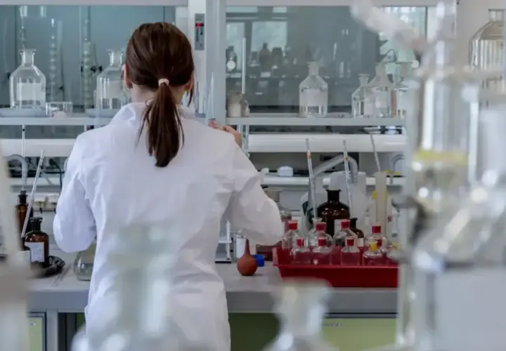 Naukowczyni w białym fartuchu pracuje w laboratorium z probówkami i odczynnikami.