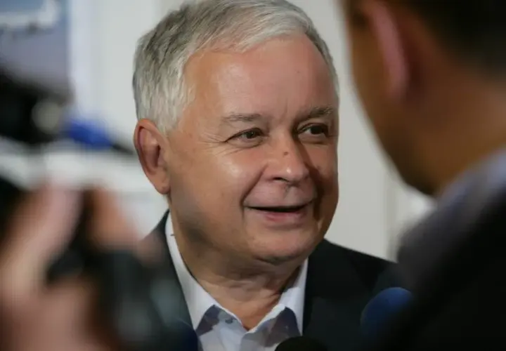 Lech Kaczyński podczas wywiadu, w tle mikrofony i niewyraźne postacie.
