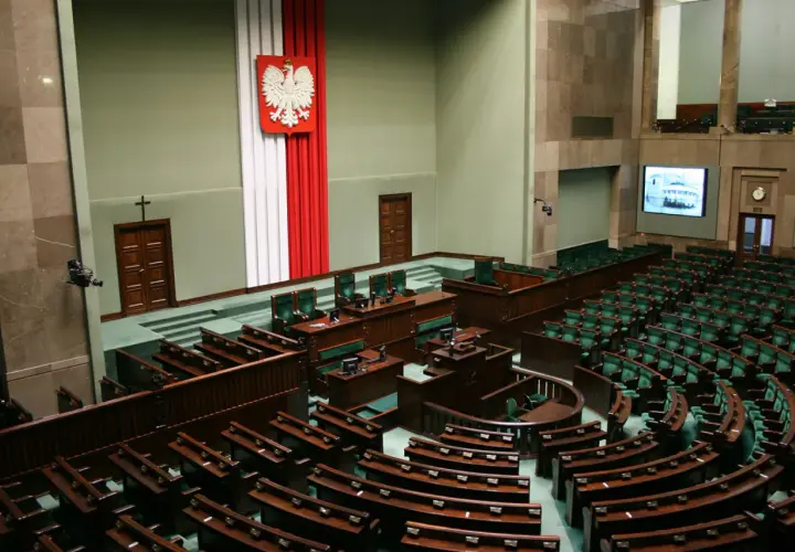 Sala plenarna Sejmu RP z godłem Polski i rzędami zielonych foteli.