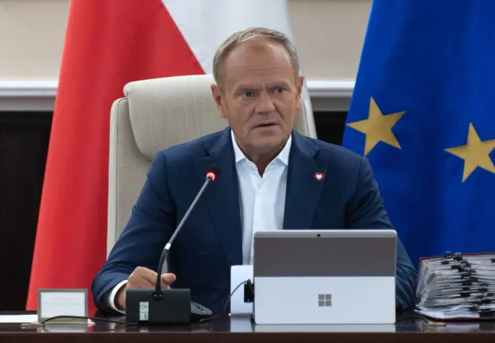 Donald Tusk siedzi przy stole, za nim flagi Polski i UE. Fani Konfederacji zarzucają rządowi "przeklejanie agendy eurokratycznej".