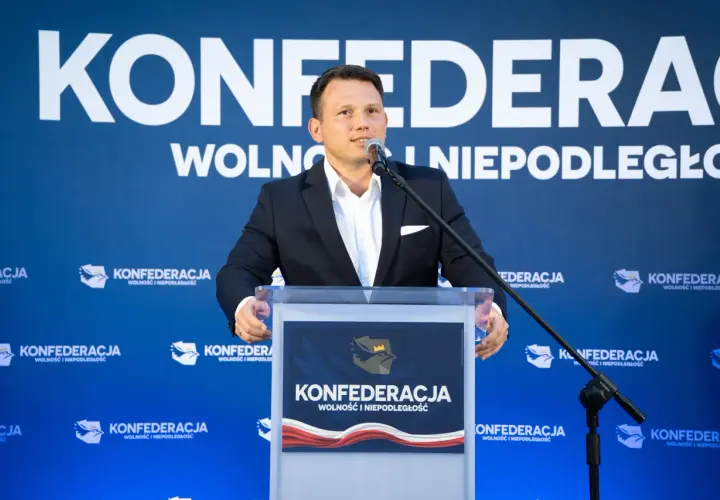 Mężczyzna w garniturze przemawia na tle logo Konfederacji. Czy to zapowiedź sekretów negocjacji Konfederacji z rolnikami w sprawie blokad granic w marcu 2026?