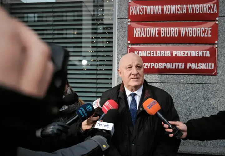 Mężczyzna przed Państwową Komisją Wyborczą, otoczony mikrofonami, mówi o prawdzie o finansowaniu kampanii PiS i decyzjach PKW o odebraniu dotacji.
