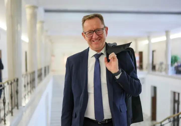 Uśmiechnięty mężczyzna w garniturze, który może być powiązany z pytaniem, dlaczego Robert Telus i Rafał Romanowski zostali zawieszeni w prawach członka.