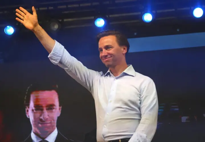 Mężczyzna w jasnej koszuli pozdrawia tłum. Na ekranie za nim widać twarz polityka, który mógłby mieć tyle lat, ile ma Bosak.