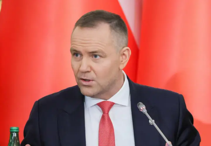 Mężczyzna w garniturze i czerwonym krawacie przemawia na tle czerwonych flag. Dyskutuje, dlaczego prezydent zapowiada veto wobec ustawy o wyborze sędziów do KRS.