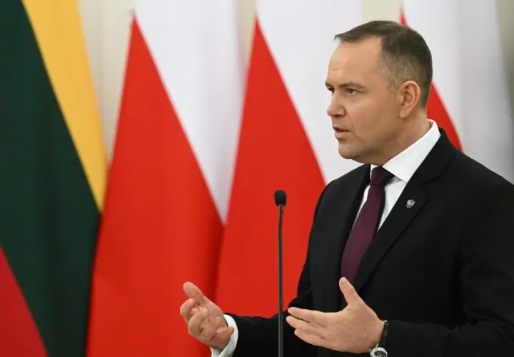 Karol Nawrocki, w garniturze, przemawia na tle flag. Jego gestykulacja i pewność siebie mogą być powodem, dlaczego Karol Nawrocki stał się nowym liderem sondaży zaufania na prawicy.