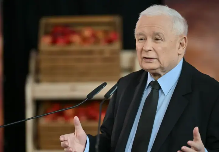 Jarosław Kaczyński w garniturze przemawia przy mikrofonach, w tle skrzynki z jabłkami.
