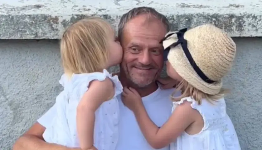 Donald Tusk z dwiema córkami całującymi go w policzki.