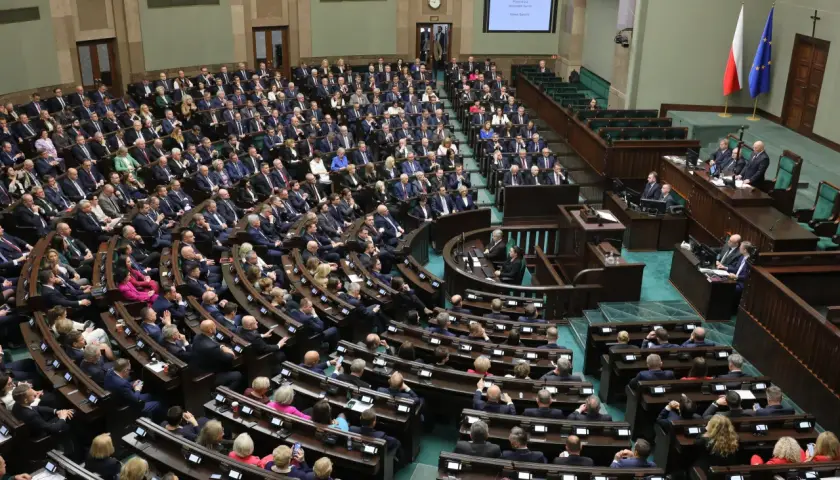 Posiedzenie Sejmu RP, wielu posłów siedzi w ławach, na mównicy przemawia mężczyzna.