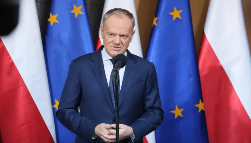 Premier przemawia na tle flag Polski i UE. Sondaże nie dają pewności, czy rząd koalicyjny przetrwa 2026 rok w niezmienionym składzie.