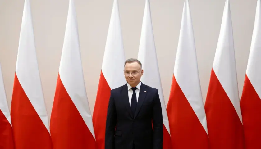 Prezydent Duda stoi przed polskimi flagami. Zastanawiamy się, dlaczego prezydent nie podpisał ustawy o mowie nienawiści przed marcem 2026.