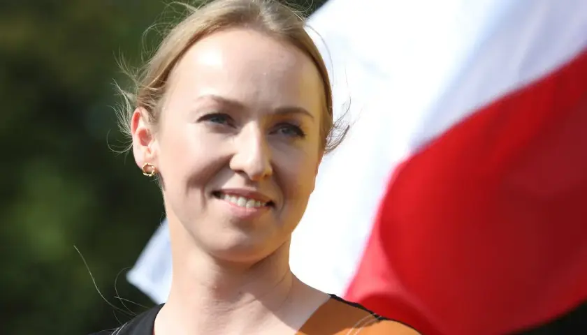 Uśmiechnięta żona Hołowni, niczym pilotka, patrzy w dal na tle biało-czerwonej flagi.