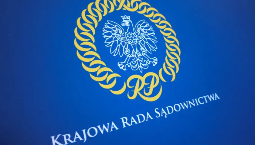 Herb RP i napis "KRAJOWA RADA SĄDOWNICTWA" na niebieskim tle. Symbolika nawiązuje do prawdziwych przyczyn konfliktu wewnątrz KO o zasady powoływania nowej KRS.